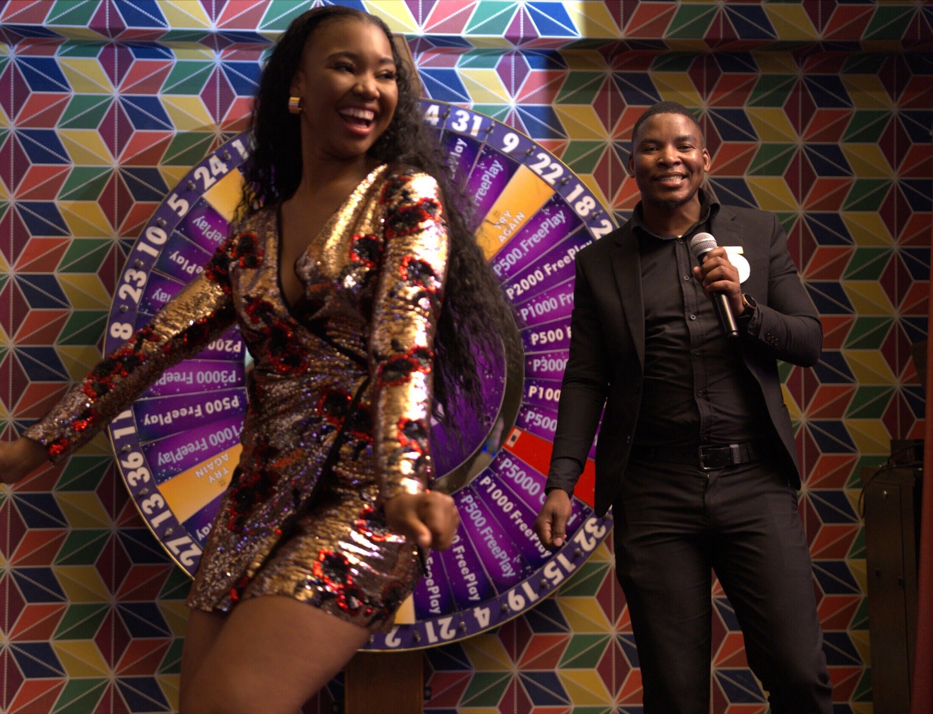 A dancer and host with microphone celebrate beside a FreePlay prize wheel at The Grand Palm, Gaborone