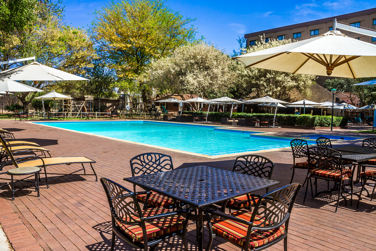 Umbrella-shaded dining tables surround the sunny outdoor pool at The Grand Palm, Gaborone