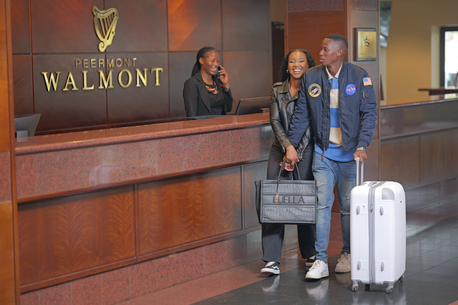 A smiling couple with luggage check in at the Walmont Hotel reception desk at The Grand Palm, Gaborone